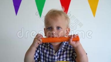 可爱的蹒跚学步的男孩<strong>双手拿</strong>着胡萝卜咬它。 万向节运动
